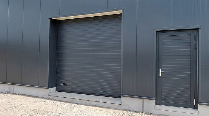 Porte sectionnelle industrielle et portillon de service sur un bâtiment bardé