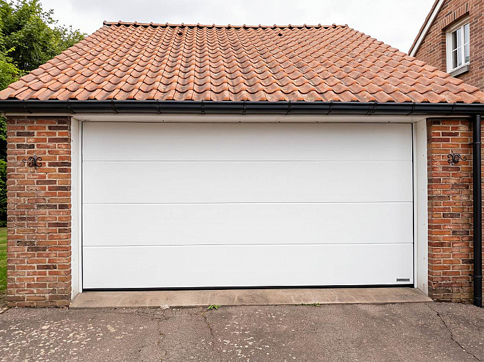 Porte de garage sectionnelle blanche posée sur une façade en brique par MFD Concept